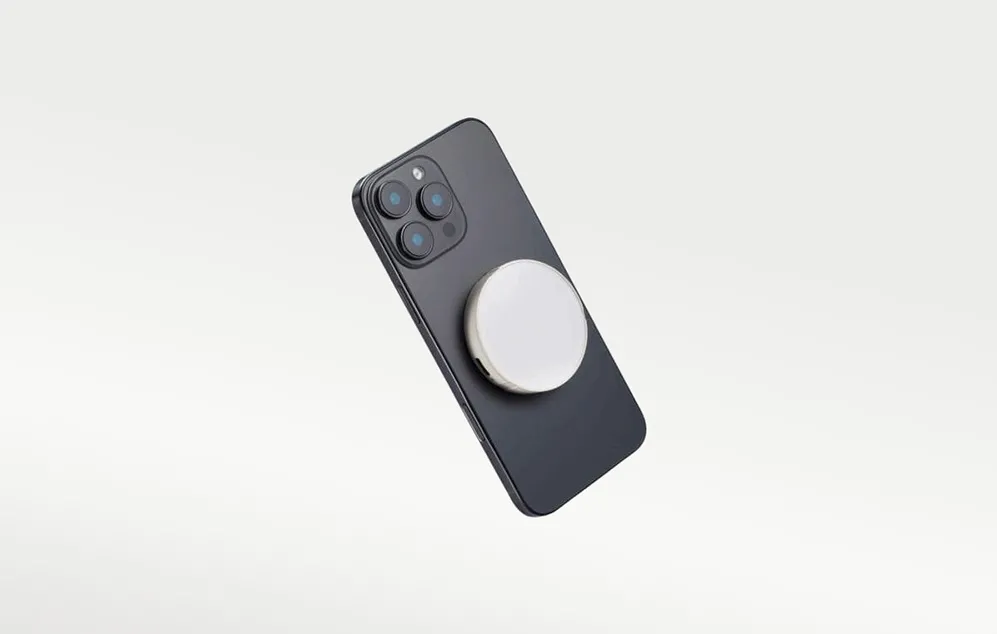 Un smartphone negru poziționat înclinat, cu o lampă LED Godox rotundă, albă, atașată magnetic