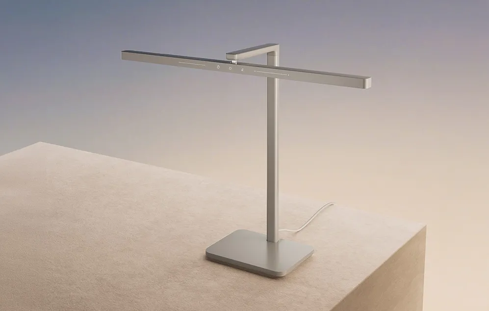 O lampă de birou LED argintie, modernă, cu un design minimalist, așezată pe un soclu bej
