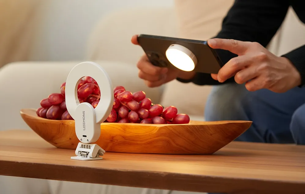 O lumină inelară albă care iluminează un bol cu struguri și un smartphone cu o lumină magnetică circulară