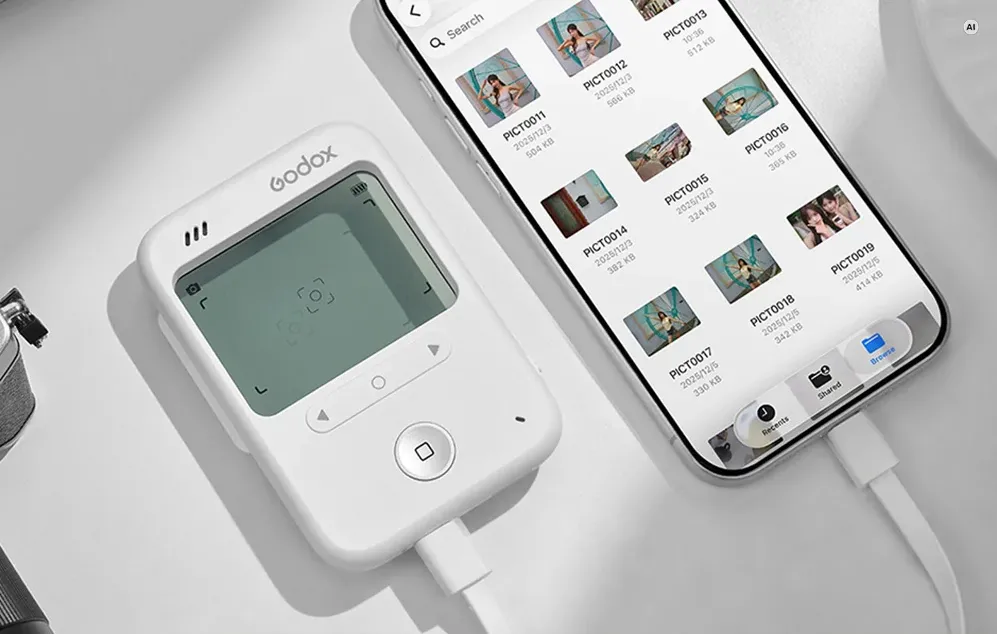Un expometru digital Godox conectat prin cablu la un smartphone care afișează o galerie foto într-o aplicație mobilă.