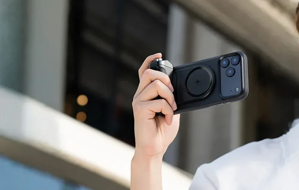 O mână ținând un smartphone cu un suport negru în timp ce face o fotografie în aer liber