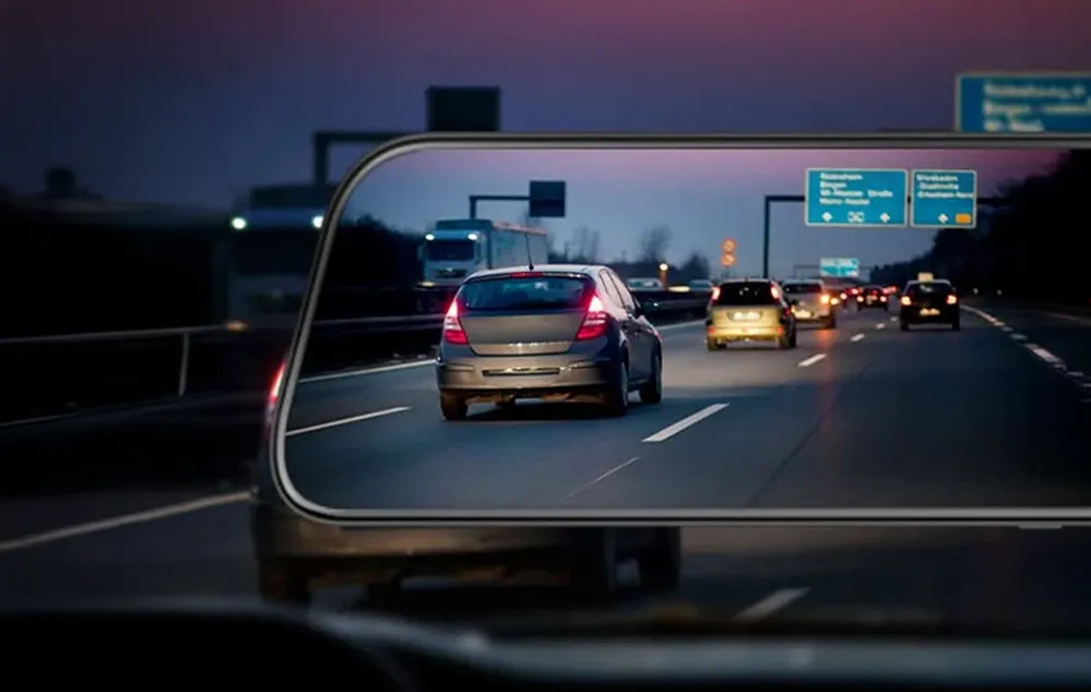 Mașini care circulă pe autostradă după lăsarea întunericului, văzute prin oglinda retrovizoare