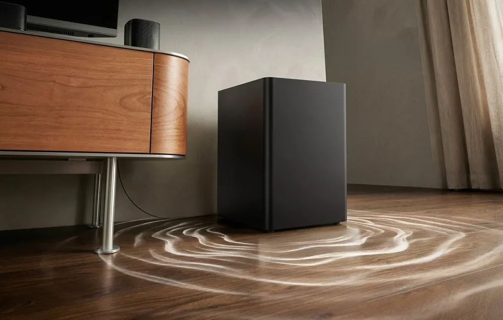 Un subwoofer negru pe o podea din lemn lângă o comodă maro
