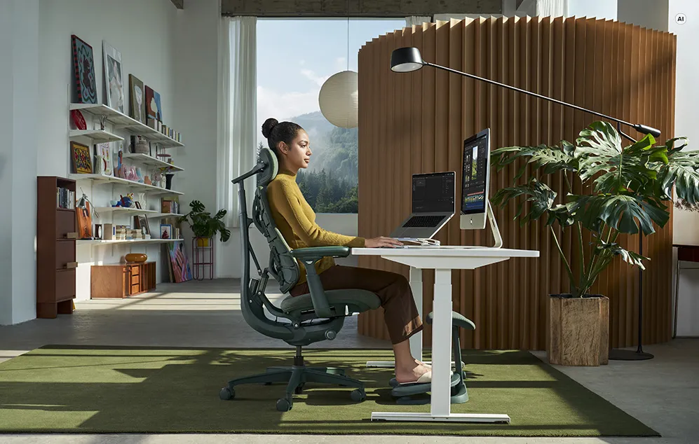 O femeie care lucrează la un birou într-un scaun ergonomic cu suport pentru picioare, prezentată în profil într-un birou.