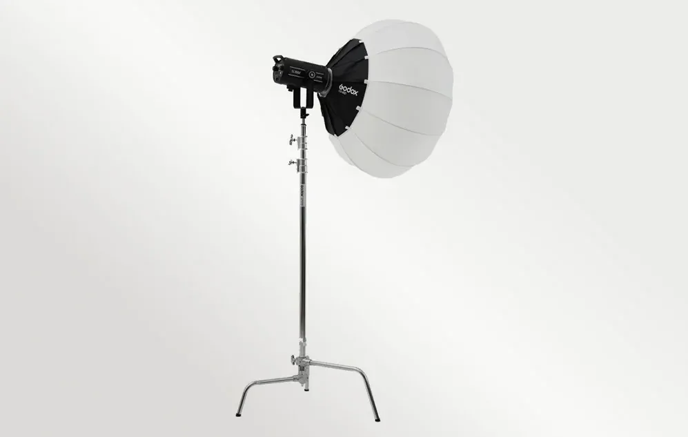 O softbox rotundă albă pe o lampă de studio neagră, montată pe un stativ de iluminat argintiu înalt, pe un fundal deschis.
