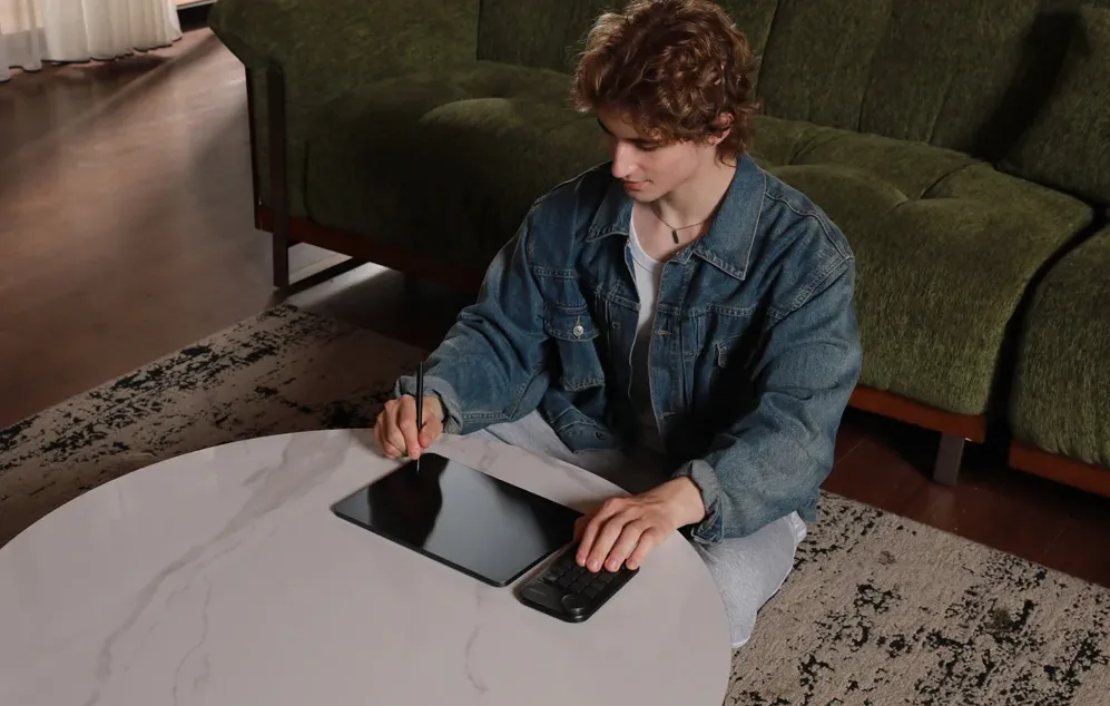 O persoană așezată la o măsuță folosește un stilou pe o tabletă conectată la o tastatură mică
