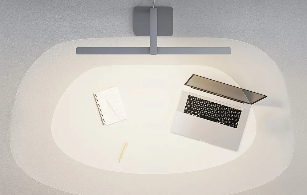 O vedere de sus a unui birou cu un laptop și un caiet scăldate în fasciculul oval și strălucitor al unei lămpi moderne