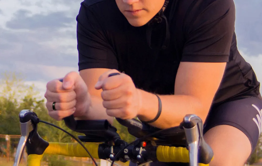 O persoană care conduce o bicicletă într-o poziție aerodinamică, cu un inel inteligent negru pe mâna stângă
